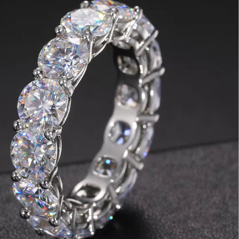 Close-up of 5 mm D-color VVS1 moissanite eternity row ring in solid 925 sterling silver with prong-set round stones, high-polish finish on a dark background — OmniVivo