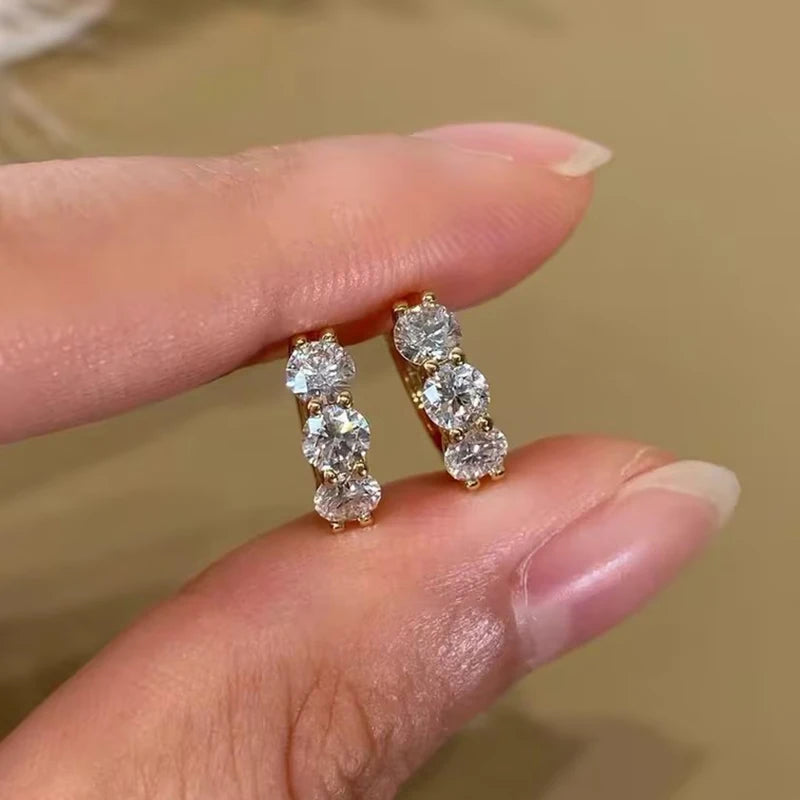 sterling silver hoop earrings plated in 14K yellow gold, set with round-cut D color VVS1 moissanite (2.5–4 mm); close-up hand shot on beige background — OmniVivo