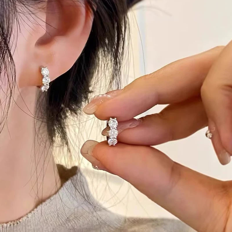 925 sterling silver hoop earring plated in 14K yellow gold, with round-cut D color VVS1 moissanite (2.5–4 mm), shown worn on ear while hand holds the second earring — OmniVivo