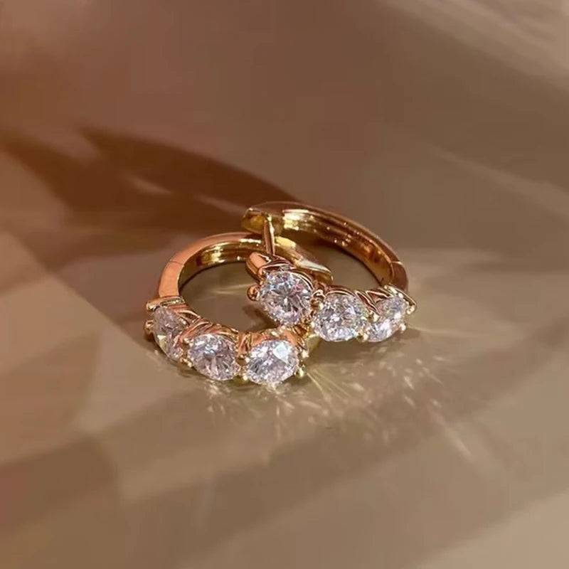 sterling silver hoop earrings plated in 14K yellow gold, set with round-cut D color VVS1 moissanite (2.5–4 mm), lifestyle photo on beige background — OmniVivo