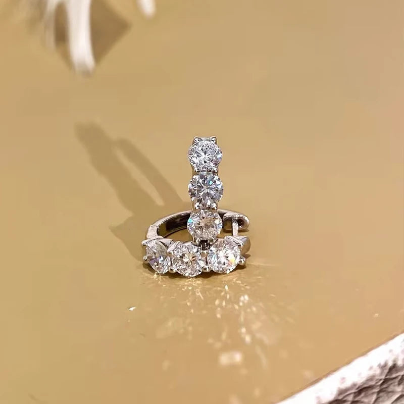 925 sterling silver hoop earring in white gold tone (rhodium finish), set with round-cut D color VVS1 moissanite (2.5–4 mm); lifestyle close-up on beige surface — OmniVivo