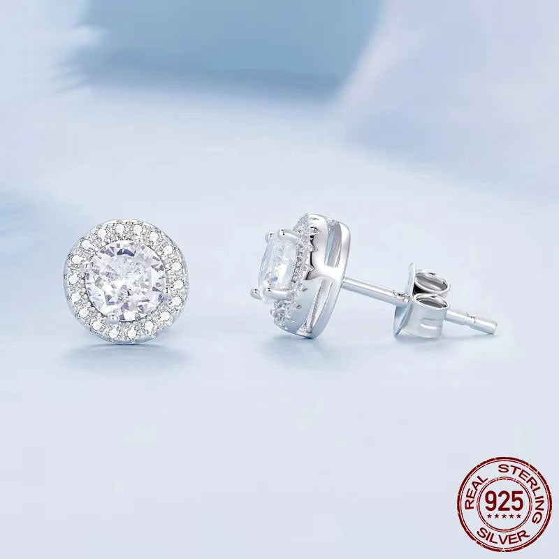A sparkling pair of Serena Halo CZ Stud Earrings in 925 sterling silver, featuring a brilliant central cubic zirconia stone encircled by a micro-pavé halo, showcasing their celestial elegance and radiant design on a soft background.