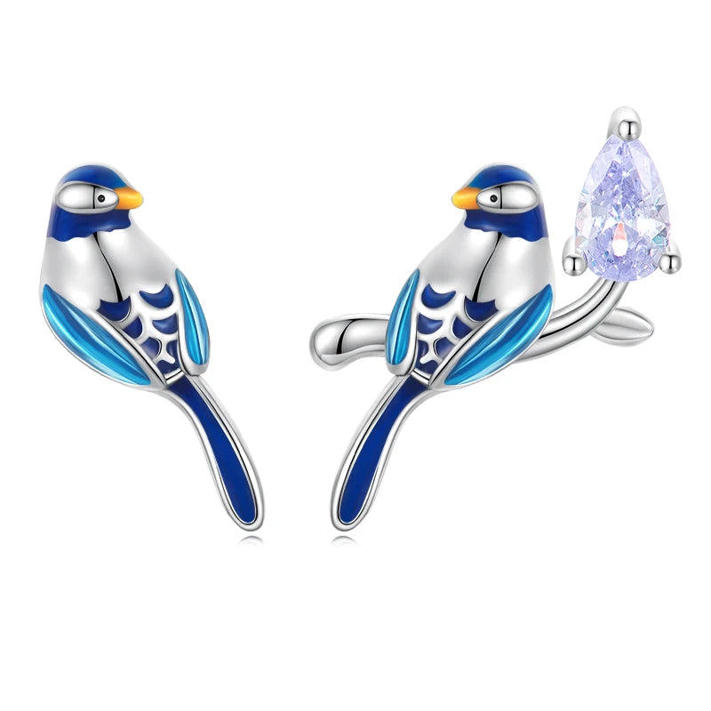 A pair of charming sterling silver bird-shaped stud earrings, featuring vibrant blue and white enamel with yellow beaks. One earring includes a sparkling dangling clear cubic zirconia teardrop, adding an elegant touch.