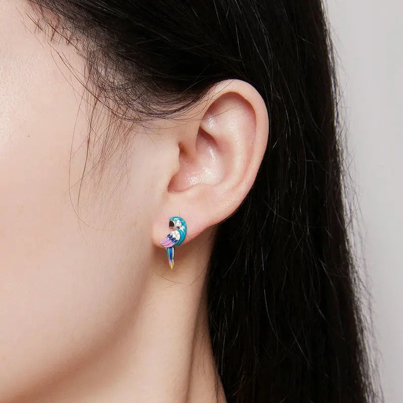 Close-up of a sterling silver parrot stud earring, featuring vibrant blue, purple, and yellow enamel details and a small sparkling cubic zirconia eye, elegantly worn on a model's ear.