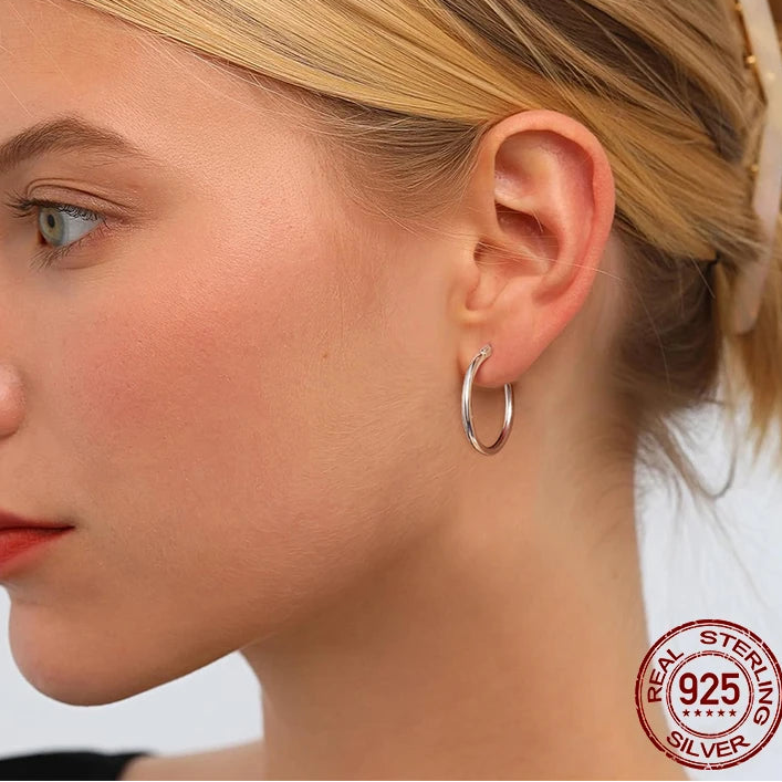 Close-up of a woman wearing glossy tube 925 sterling silver hoop earrings, 14K white gold plated, on-ear lifestyle — OmniVivo