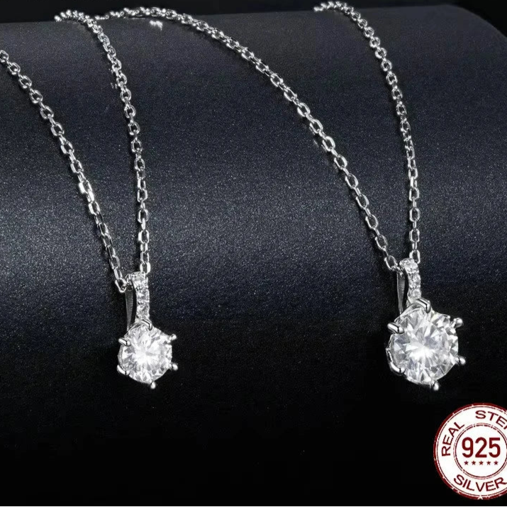 Two 1ct D color VVS1 moissanite solitaire pendant necklaces on 925 sterling silver chains, close-up on black display with 925 stamp