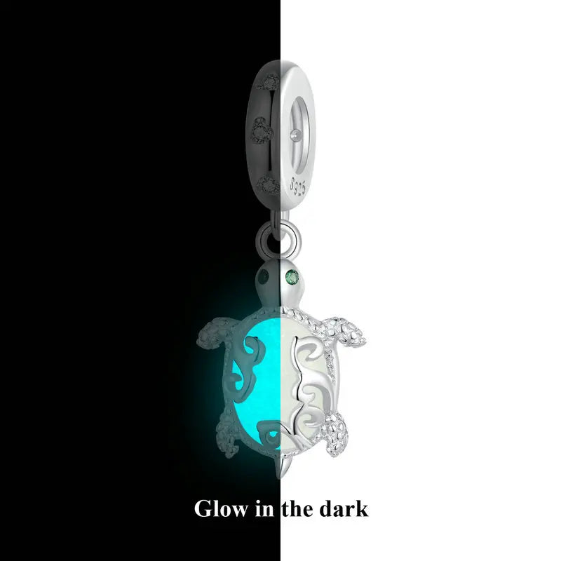 Glow-in-the-dark turtle charm in 925 sterling silver with luminous blue core, studio half black–half white background.
