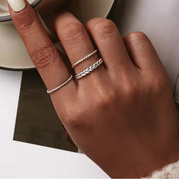 Lifestyle close-up of a hand wearing braided and twisted 925 sterling silver stacking rings on a neutral background — OmniVivo