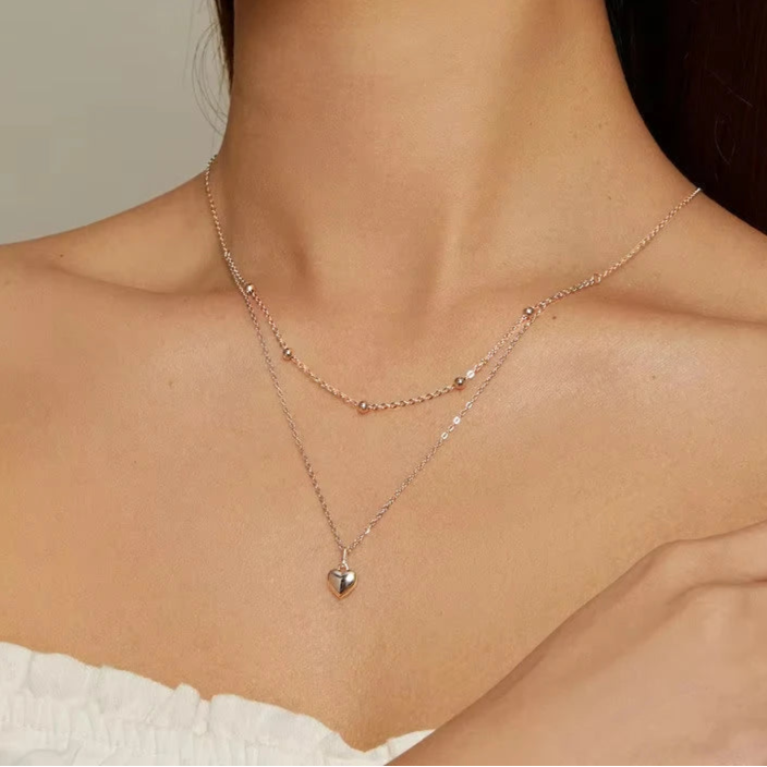 Close-up of a silver-tone double-layer 925 sterling silver heart pendant necklace with beaded station and link chains, worn on neck — OmniVivo