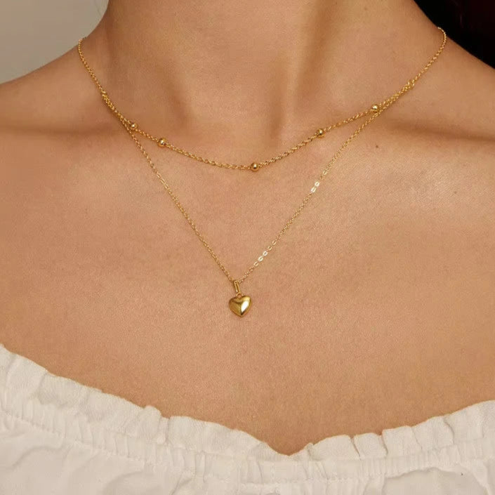 Close-up of a gold-tone double-layer 925 sterling silver heart pendant necklace with beaded station and link chains, worn on neck — OmniVivo