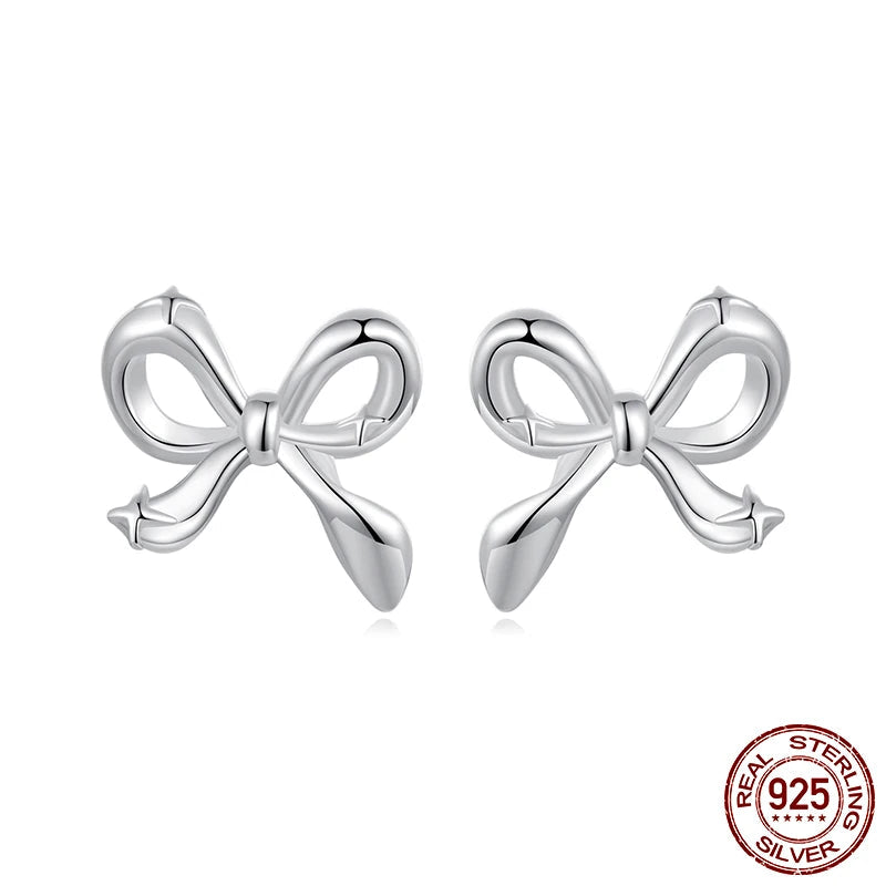Close-up of mini bow stud earrings in 925 sterling silver with white-gold plating, ribbon knot design on white background — OmniVivo