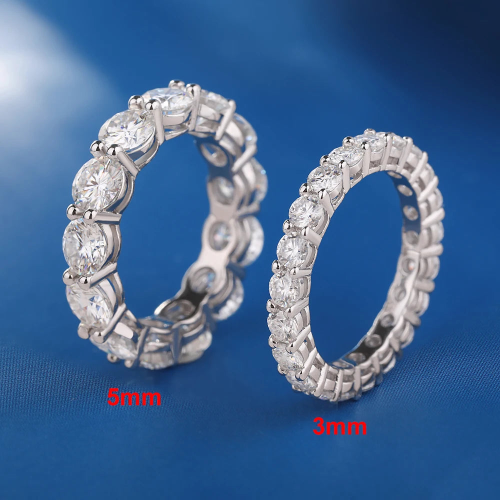Two D-color VVS1 moissanite eternity row rings (5 mm and 3 mm) in solid 925 sterling silver with prong-set round stones on a blue background — OmniVivo