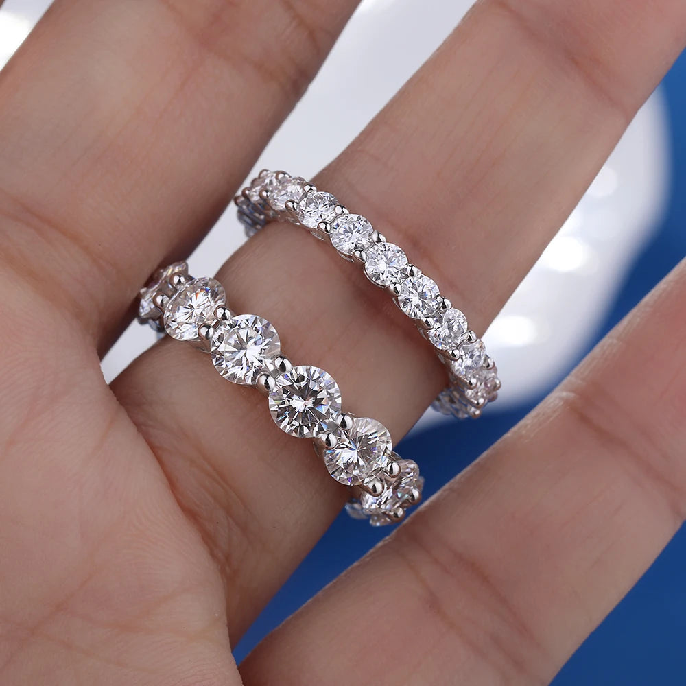 Two D-color VVS1 moissanite eternity row rings (5 mm and 3 mm) in solid 925 sterling silver, shown on fingers against a blue background — OmniVivo