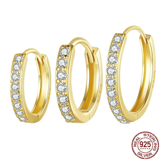 A set of three sparkling gold-plated 925 sterling silver huggie hoop earrings, each featuring a line of brilliant cubic zirconia stones, displayed against a white background. Perfect for everyday elegance or cartilage piercings.
