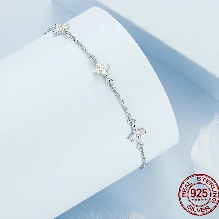 925 sterling silver anklet with star and floral charm details, delicate adjustable chain shown in an angled studio display on a light blue background with visible 925 stamp — OmniVivo
