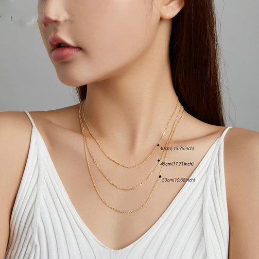 A model elegantly showcasing three different lengths of Alina gold-toned chain necklaces: 40cm (15.75in), 45cm (17.71in), and 50cm (19.68in), highlighting the adjustable options for layering and versatile styling.