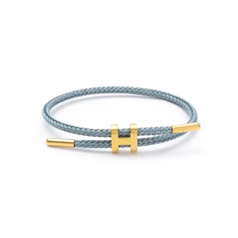 Gray braided rope bracelet with a sleek gold bar clasp, minimalist unisex design, lightweight and stackable, studio shot on a clean white background — OmniVivo