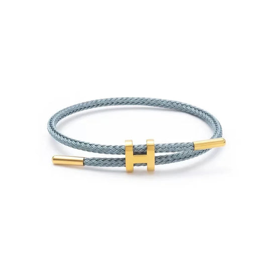 Gray braided rope bracelet with a sleek gold bar clasp, minimalist unisex design, lightweight and stackable, studio shot on a clean white background — OmniVivo