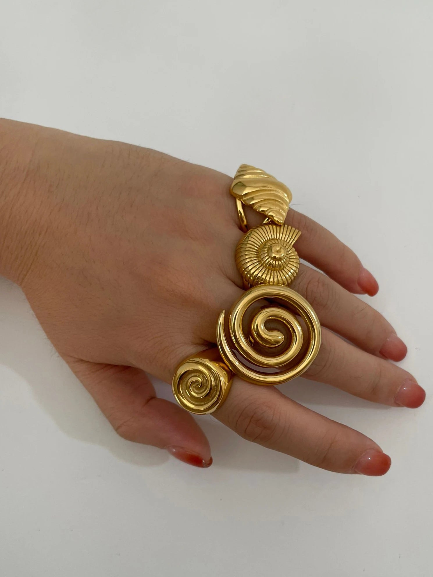 Stacked conch croissant spiral open rings in glossy 18K gold–plated stainless steel, bold chunky summer statement shown on hand against white background — OmniVivo