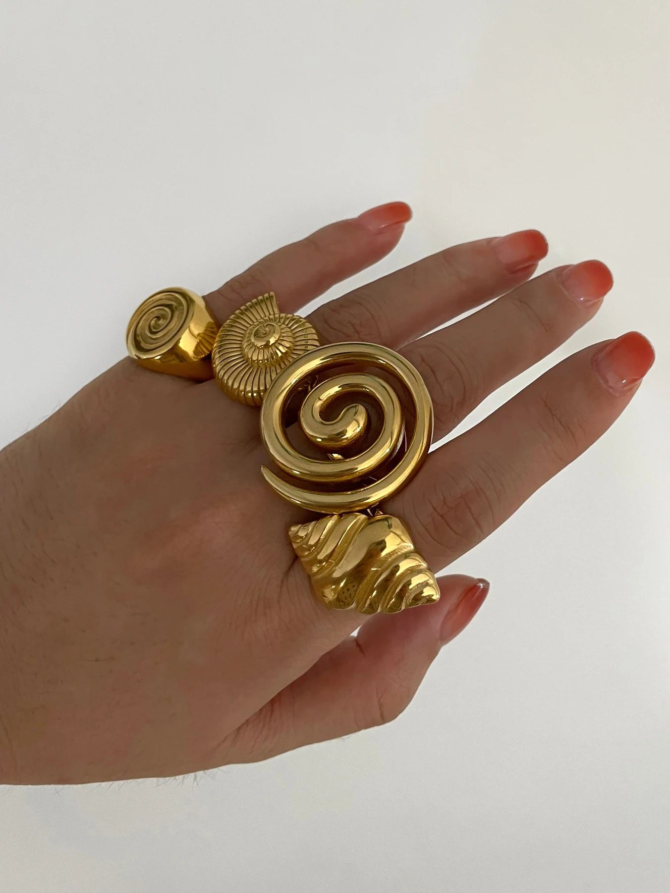 Chunky conch croissant spiral open ring, glossy 18K gold–plated stainless steel, bold summer statement shown stacked on hand, lifestyle close-up — OmniVivo