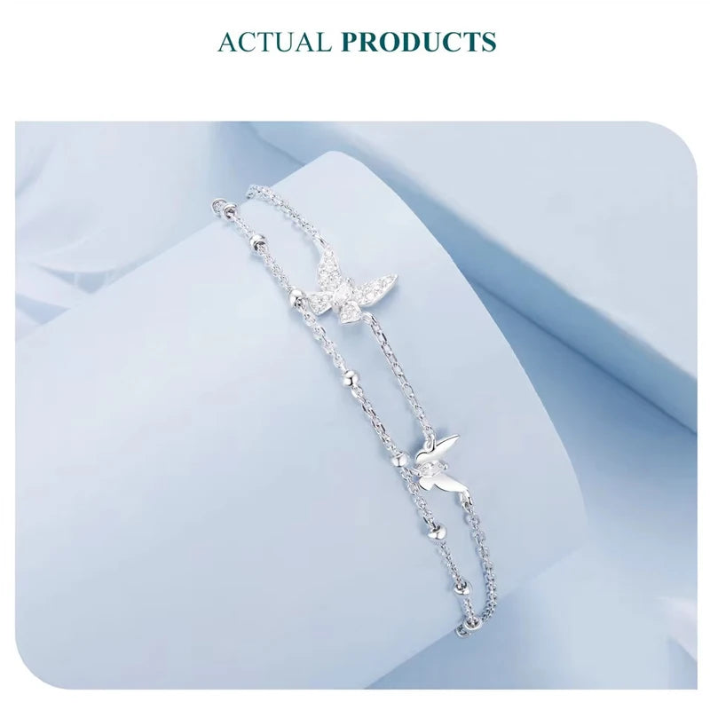 Double-layer butterfly bracelet in 925 sterling silver with pavé CZ, dainty layered chains displayed on soft light-blue fabric with adjustable extender — OmniVivo