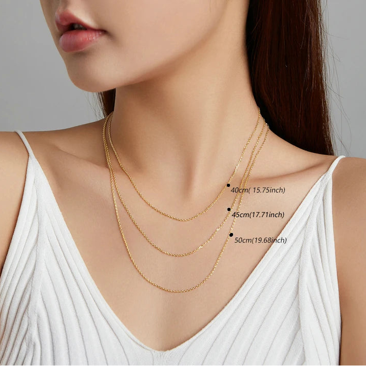 Model wearing layered gold-tone necklace chains at 40, 45, and 50 cm lengths, minimalist studio background — OmniVivo