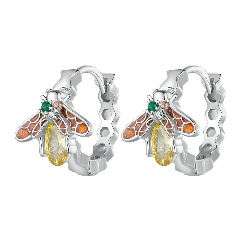 A charming pair of sterling silver hoop earrings featuring an intricate honeycomb pattern. Each earring is adorned with a colorful enamel bee, accented with small green and clear cubic zirconia, and a dangling yellow teardrop crystal, perfect for nature lovers.