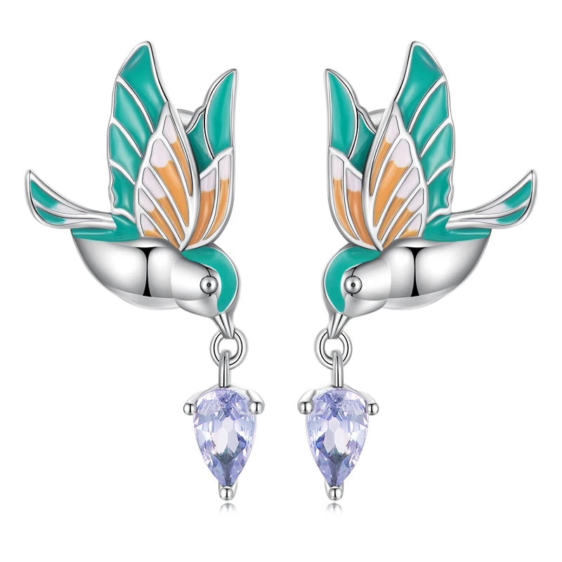 A pair of exquisite sterling silver dangling bird earrings, featuring vibrant green and orange enamel wings, with each bird holding a sparkling purple teardrop cubic zirconia, perfect for a whimsical yet elegant statement.
