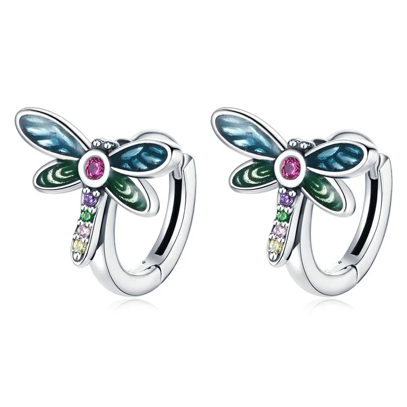 A charming pair of sterling silver dragonfly-shaped hoop earrings, featuring blue and green enamel wings, a pink central crystal, and a line of colorful cubic zirconia stones on the body, perfect for a whimsical and vibrant look.