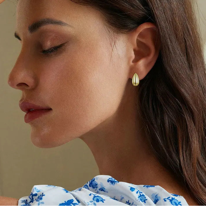 Model wearing gold-plated 925 sterling silver glossy teardrop earrings, on-ear close-up with soft studio background — OmniVivo