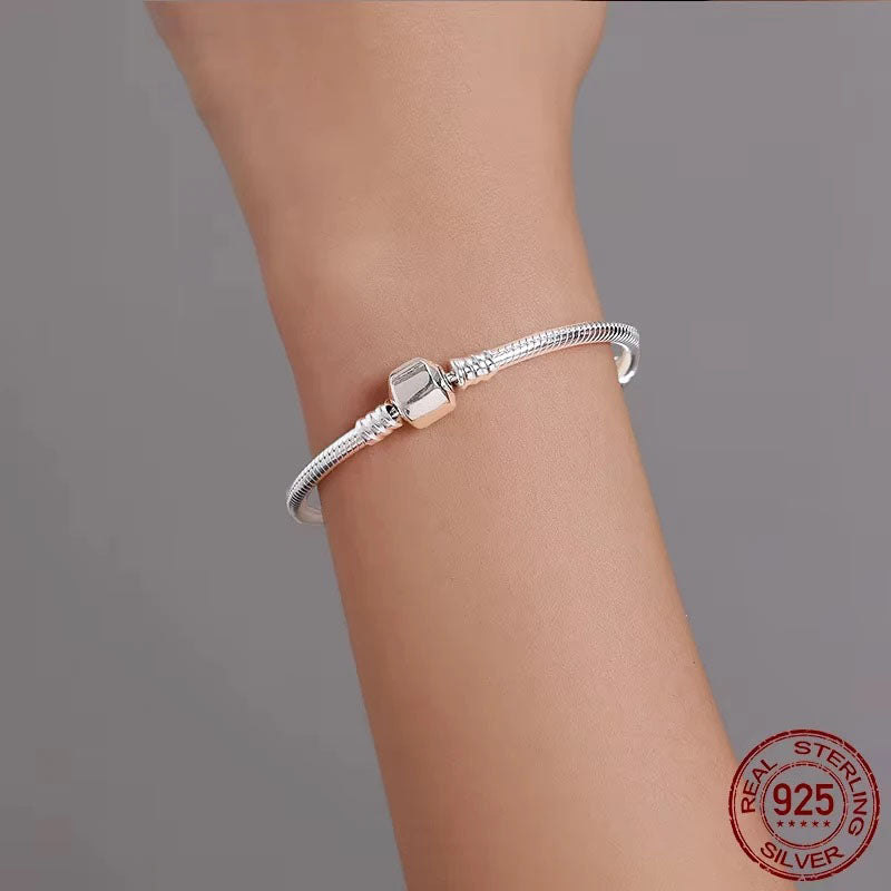 A model's arm elegantly displaying a Vespera 925 sterling silver snake chain bracelet, featuring a smooth, high-polish finish and a secure barrel clasp, showcasing its luxurious and adaptable fit.