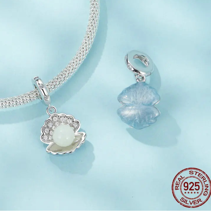 Set of glow-in-the-dark ocean charms in 925 sterling silver—a shell with luminous bead, crescent moon with cat, and star bottle with dangling star—front view on white background.