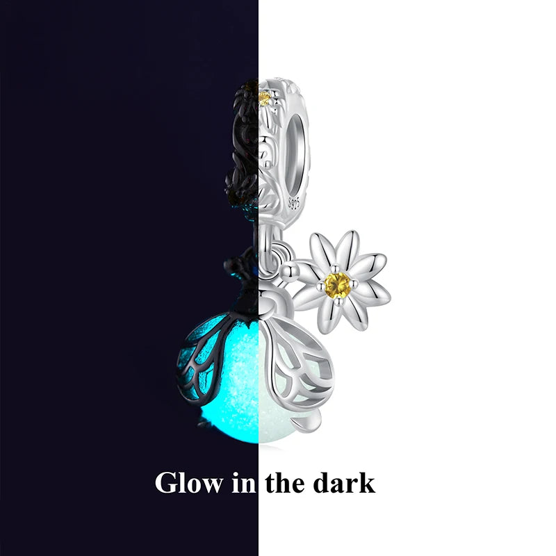 Glow-in-the-dark flower charm in 925 sterling silver with luminous blue bead and daisy detail, studio split black–white background.