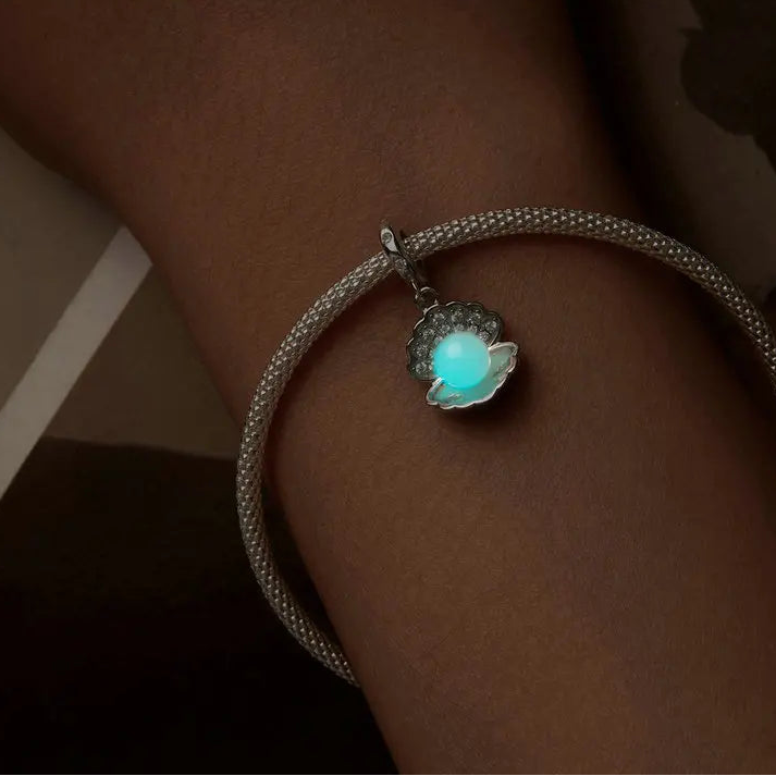 Glow-in-the-dark shell charm in 925 sterling silver on a bracelet, worn on wrist against a dark background.