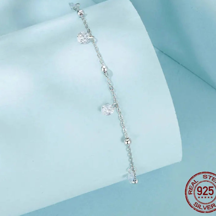 925 sterling silver cubic zirconia anklet with adjustable extender and dangling charms — detail shot on light blue background with 925 stamp.