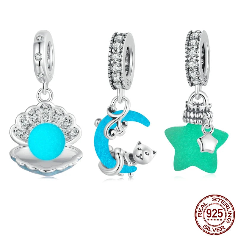 Set of glow-in-the-dark ocean charms in 925 sterling silver—a shell with luminous bead, crescent moon with cat, and star bottle with dangling star—front view on white background.