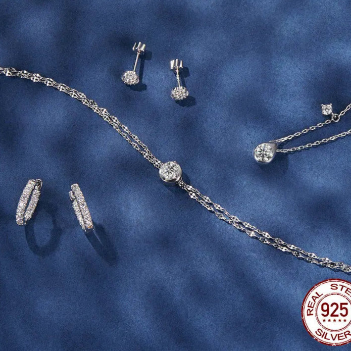 Moissanite hoop earrings in 925 sterling silver shown in a jewelry set flatlay on a blue background.