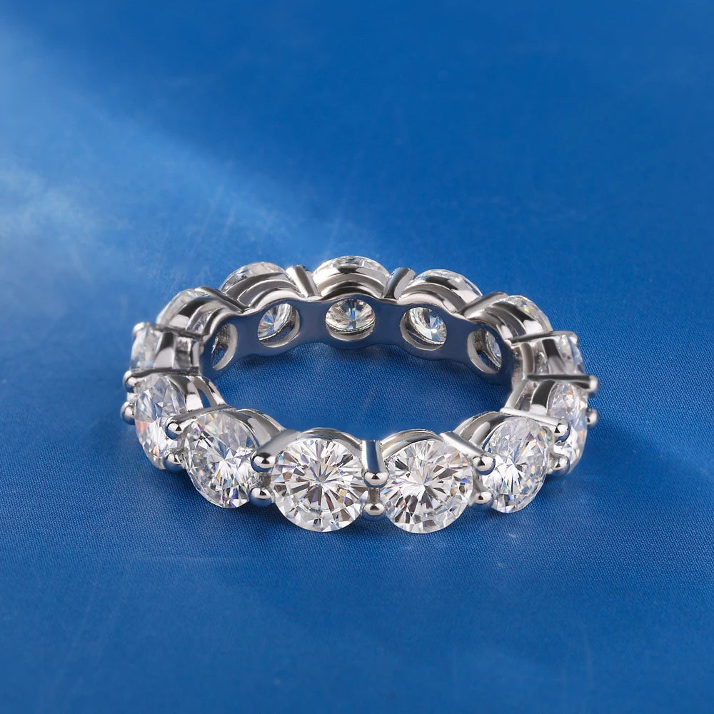 Close-up of a 5 mm D color VVS1 moissanite row ring in solid 925 sterling silver, prong-set eternity band on a blue background.