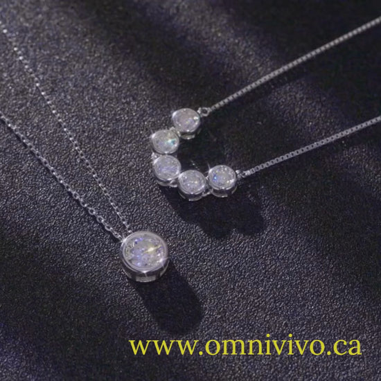 Showcase video of 1ct (6.5 mm) D color VVS1 moissanite bezel pendant necklace in authentic 925 sterling silver, plus multi-bezel bar necklace, on a dark background — OmniVivo