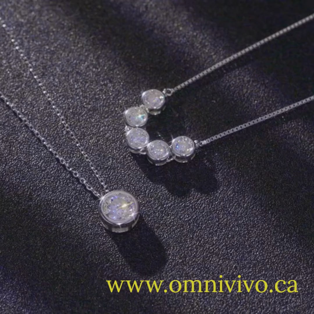 Showcase video of 1ct (6.5 mm) D color VVS1 moissanite bezel pendant necklace in authentic 925 sterling silver, plus multi-bezel bar necklace, on a dark background — OmniVivo