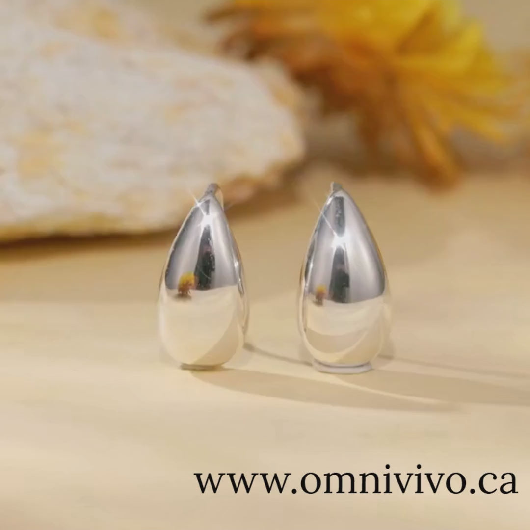 Glossy teardrop earrings in 925 sterling silver, 15×8 mm waterdrop design, shown on a warm floral backdrop — OmniVivo
