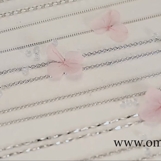 Assorted 925 sterling silver necklace chains with lobster/O-link styles, studio flat-lay on a soft floral backdrop — OmniVivo