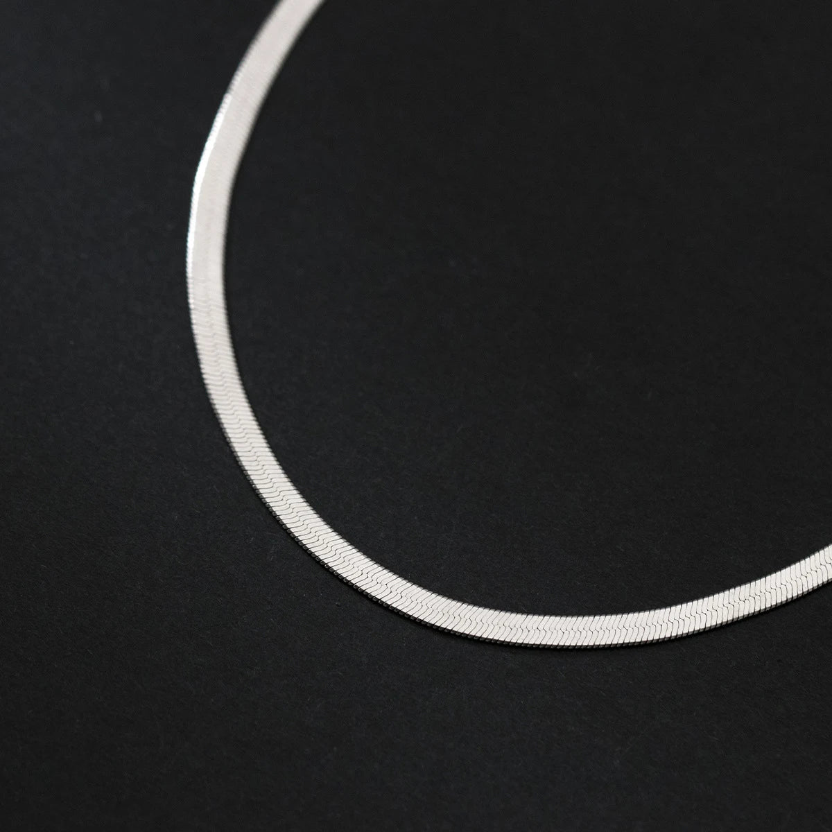 Close-up of silver-tone snake chain anklet in 925 sterling silver, textured detail on a black background.