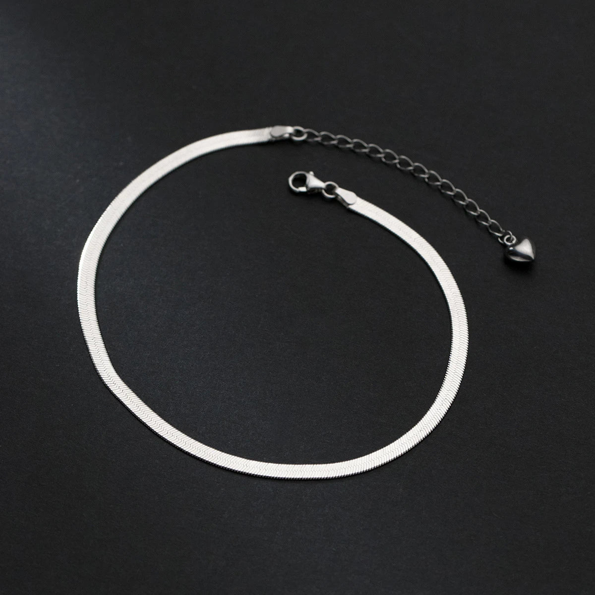 Silver-tone snake chain anklet in 925 sterling silver on a black background, adjustable extender.